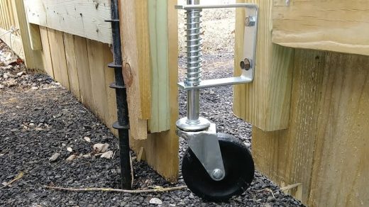 Close-up of a spring-loaded gate wheel attached to a wooden gate, showing its robust metal construction and functionality for supporting heavy gates.